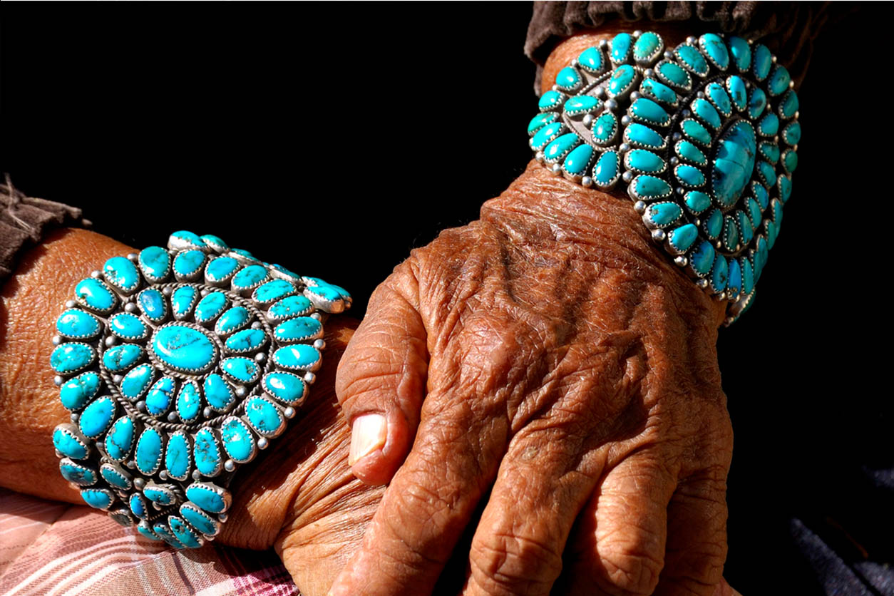 two hands of an older person, wearing a bracelet on each arm, turqoise native pieces